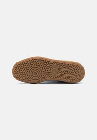 Gummisula till sneakers med ett cirkulärt och linjärt däckmönster. Färg: ljusbrun. Accentuerad med en logotyp nära hälen.