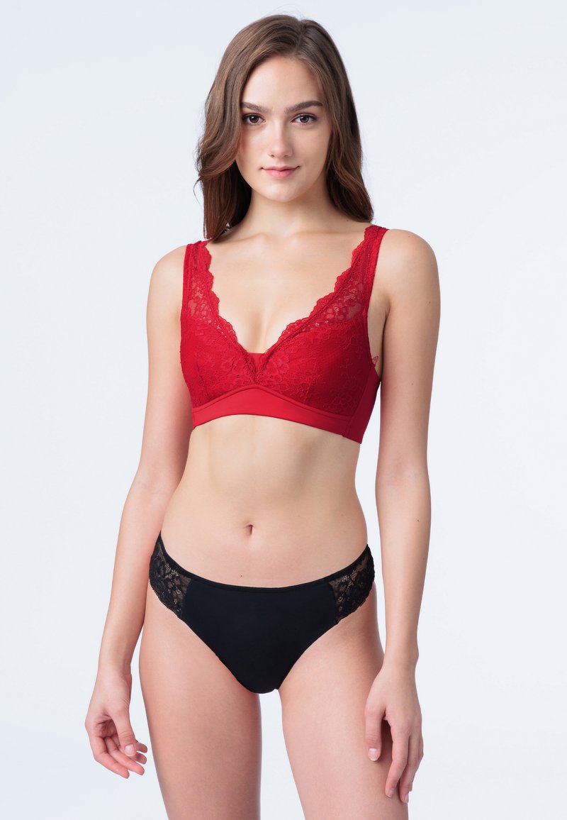 Bralette rossa in pizzo con scollatura profonda e spalline larghe in pizzo, abbinato a slip bikini neri con dettagli in pizzo sui lati.