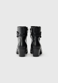 Bottines noires en cuir lisse, avec un bout rond, un talon modeste, une fermeture éclair sur le côté et un détail de sangle réglable.