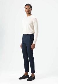 Lichtbeige shirt met lange mouwen, marineblauwe op maat gemaakte broek en donkere loafers. Gladde texturen en een getailleerd ontwerp, staand tegen een effen achtergrond.