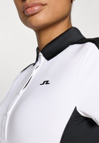 Λευκό πόλο μπλουζάκι με μαύρο ριμπ γιακά και διακοσμητικά στους ώμους, με μπροστινό ημι-φερμουάρ και μικρό μαύρο λογότυπο στο στ�ήθος.