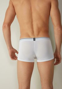 Weiße Boxershorts aus dehnbarem Stoff mit schmalem schwarzen Bund. Glatte Textur, enganliegendes Design und minimale Markenkennzeichnung am Bund.