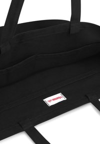 Zwarte canvas schoudertas met twee handvatten, met een ruime binnenkant en één binnenzak. Label met "WannaSik" branding zichtbaar.