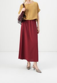 Haut à manches courtes moutarde, coupe ample, associé à une jupe bordeaux longue jusqu'aux chevilles. Sac à main gris et ballerines pointues grises complètent la tenue.