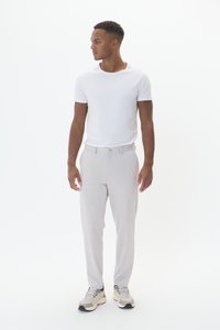 Chemise blanche à manches courtes, pantalon gris clair et baskets grises. Le pantalon est doté d'une ceinture, d'une texture lisse et d'une coupe ajustée.