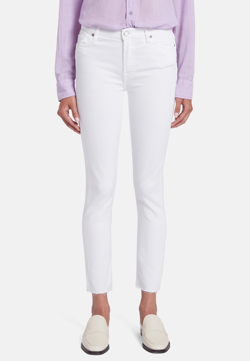 Jeans skinny en denim blanc avec un ourlet brut, présentant un design classique à cinq poches et des accents métalliques. Associés à un blouse de couleur lilas.
