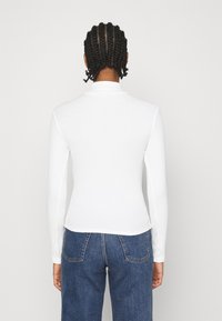 Witte geribbelde top met lange mouwen en een hoge kraag, met een aansluitende pasvorm en subtiele textuur, gecombineerd met blauwe spijkerbroek.