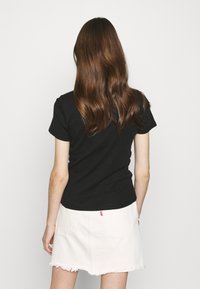 T-shirt nera a maniche corte con una forma aderente, abbinata a una gonna di jeans bianca con bordi sfilacciati e un piccolo etichetta rossa sul retro.