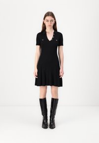 Black ribbed dress with short sleeves, V-neck, and decorative buttons at the collar. Paired with knee-high black boots.