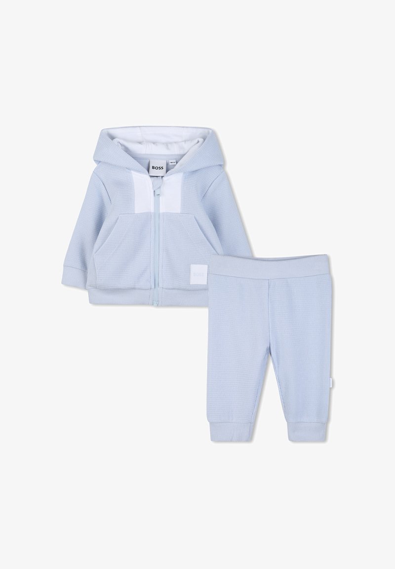 Ensemble de survêtement bleu clair comprenant une veste à capuche zippée avec une finition texturée et un pantalon assorti avec une taille élastiquée.