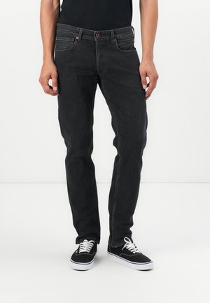 Sorte jeans i denim med slank passform, fem lommer og brune knappdetaljer, parret med sorte sneakers og hvite snører.
