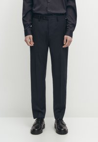 Pantaloni blu navy con vestibilità dritta, realizzati in un tessuto liscio. Presentano una vita con passanti per cintura e sono abbinati a scarpe nere.
