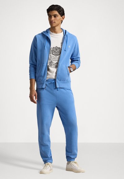Ανοιχτό μπλε φούτερ με μπροστινές τσέπες, σε συνδυασμό με ταιριαστά joggers και ένα γραφικό t-shirt από κάτω. Τα αθλητικά παπούτσια ολοκληρώνουν την εμφάνιση.