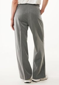 Pantaloni grigi a gamba larga realizzati in un tessuto leggero e testurizzato. Presentano una finitura liscia e due tasche posteriori. Abbinati a sneaker bianche.