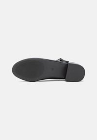 Black leather shoe sole with a smooth surface and ribbed texture. Features a small block heel and a rounded toe design.