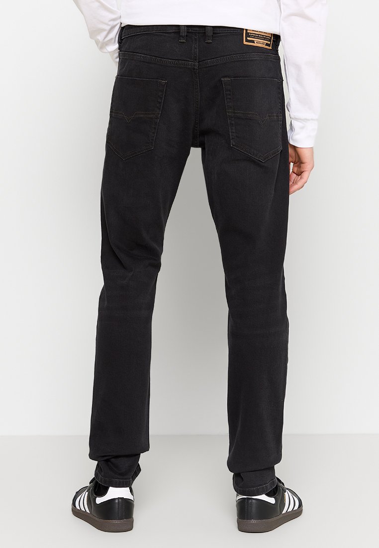Jean en denim noir à coupe slim, doté de cinq poches, de coutures visibles et d'un patch en cuir de marque sur la ceinture.