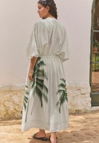 Light green maxi dress with short puff sleeves, elastic waist, and palm leaf print along the skirt, made from a textured fabric.
