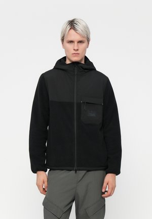 Black fleece jacket with a zip front, hood, and a chest pocket. Features a contrasting panel design and textured fabric. Worn with gray cargo pants.