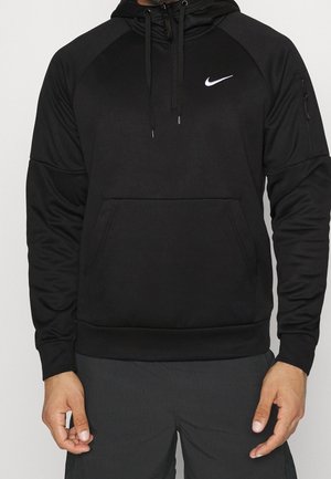 Mężczyzna w czarnej bluzie Nike z kapturem z kieszenią kangurzą i kieszenią na suwak na lewym rękawie, w połączeniu z ciemnymi spodniami.