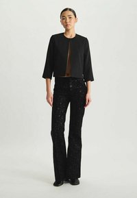 Veste noire courte avec un col rond et des manches trois-quarts ; assortie à un pantalon noir évasé avec un motif texturé et pailleté.