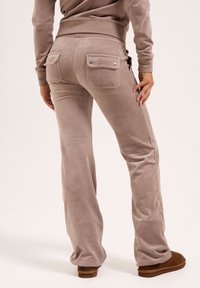 Braun-graue, ausgestellte Hose aus weichem Material, mit zwei Gesäßtaschen und metallischen Akzenten, von hinten gezeigt.