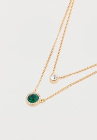 Colier cu straturi de ton auriu, având două pandantive: o piatră verde mare înconjurată de cristale clare și o piatră clară mai mică. Textura lanțului este netedă.