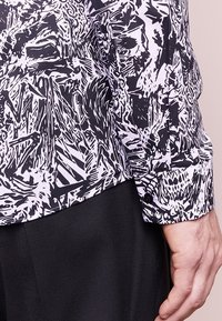 Black and white patterned shirt with a smooth fabric, featuring a pointed collar, buttoned cuff, and abstract designs on the sleeve.