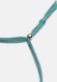 Tyrkysové bavlněné nitě svázané do uzlu s lesklou kovovou kulatou korálkou jako akcentem, což vytváří jednoduchý, minimalistický design.
