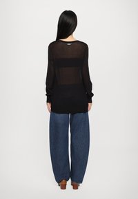 Must musta, läbipaistev pikkade varrukatega topp ümmarguse kaelusega, kantud lahtiste, kõrge vöökohaga siniste teksade peal. Minimalistlik disain ja lõdva istuvuse puhul.