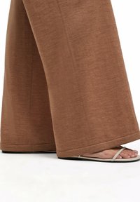 Bruine wijde broek in een gestructureerde stof, met een losse pasvorm. De outfit is gecombineerd met beige slippers met een eenvoudig ontwerp.