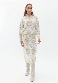 Stickad tröja och midiklänning i krämfärg med beige diamantmönster. V-ringning, ribbade ärmslut och knähöga beige stövlar. Slät textur.