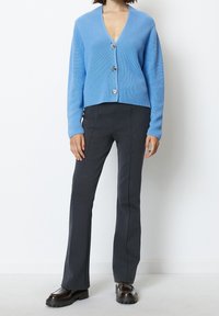 Ljusblå ribbade stickade cardigan med V-ringning, utrustad med tre knappar. Kombinerad med mörka raka byxor och grova svarta skor.