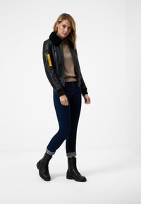 Black leather bomber jacket with a faux fur collar, featuring a yellow zipper pocket on the sleeve. Paired with dark jeans and black combat boots.