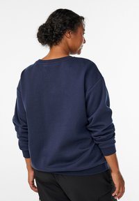 Tamsiai mėlynas džemperis su laisvu siluetu, nerta rankogalių ir apvalia iškirpte. Minkšta tekstūra, detalės matomos ant nugaros ir rankovių.