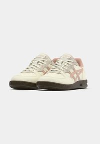 Kremo spalvos sportbačiai su rožiniais ir pilkais akcentais, viršus iš odos ir tekstilės, perforuotas pirštų srityje, rudas gumos padas. Ant liežuvėlio – firminis logotipas.