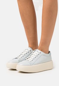 Baskets en cuir bleu clair avec un bout arrondi, des lacets blancs et une semelle plateforme épaisse crème. Présentent des coutures discrètes et un design minimaliste.