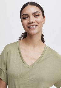Maslinasto zeleni T-shirt s V izrezom i kratkim rukavima, izrađen od mekanog, rebrastog materijala, s ležernim krojem i glatkom teksturom.