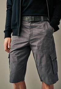 Graue Cargo-Shorts aus leichtem Material, mit Seitentaschen, Gürtelschlaufen und lockerer Passform. Texturierte Oberfläche mit dezentem Glanz.