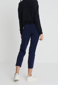 Marineblauwe cropped broek met een strakke pasvorm, gladde stof en een middenhoge taille. Gepaard met witte sportsneakers, gezien vanuit de achterkant.