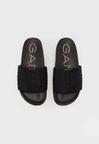 Sandale negre cu talpă plată, având un design împletit pe curea, caracterizate printr-o talpă netedă și logo-uri aurii embossate pe interior.