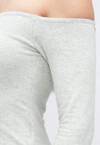 Gaiši pelēks topiņš bez plecu daļas, izgatavots no mīksta, elastīga auduma ar pieguļošu dizainu, bez redzamiem rakstiem vai akcentiem.