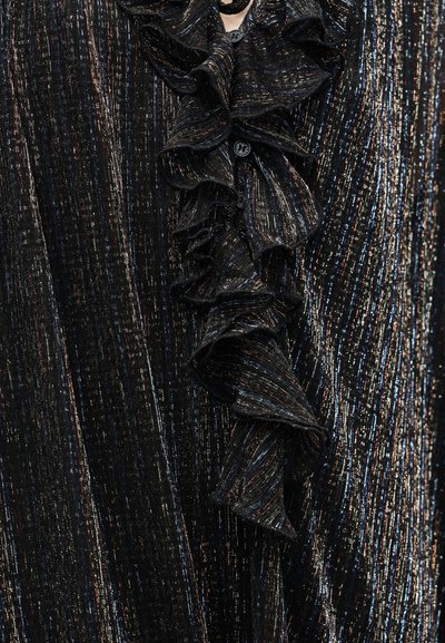 Μαύρο, υφασμάτινο ύφασμα με υφή, μεταλλικές λεπτομέρειες και κάθετες ρίγες. Διαθέτει γιακά με βολάν και διακοσμητικό κουμπί στο λαιμό.