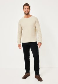 Beiges, geripptes Langarmshirt mit Rundhalsausschnitt, kombiniert mit schwarzen, gerade geschnittenen Hosen und braunen Schnürschuhen. Einfaches Design, strukturierter Stoff.