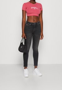 Růžové zkrácené tričko s logem "Tommy Jeans", šedé slim džíny, černá kabelka a bílé tenisky. Jednoduchý design, těsný střih a minimální detaily.