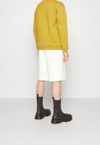 Żółta bluza, białe szorty do kolan i czarne skórzane botki za kostkę z grubą podeszwą. Prosty design, teksturowana tkanina i jednolite kolory.