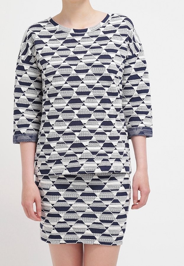 Femme portant une robe ajustée à manches trois-quarts, arborant un motif géométrique de triangles bleu marine et blanc.