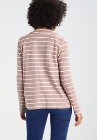 Långärmad skjorta i ett mjukt, strukturerat tyg med horisontella ränder i ljusrosa och krämfärg. Rund halsringning och avslappnad passform.