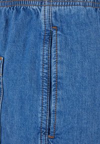 Džinsinis audinys, pasižymintis mėlyna spalva su lygiu paviršiumi, pabrėžiamas kontrastinėmis rudos spalvos siūlėmis ir vertikaliu kišenės atidarymu.