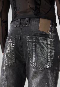 Črne jeans hlače iz denima z teksturiranim, kovinskim leskom. Imajo zadnje žepe in rjav usnjeni pečat. Vključujejo vidne šive.