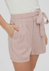 Ljusrosa shorts med knytband i midjan, sidofickor och en texturerad tyg. Har veck och en avslappnad passform.